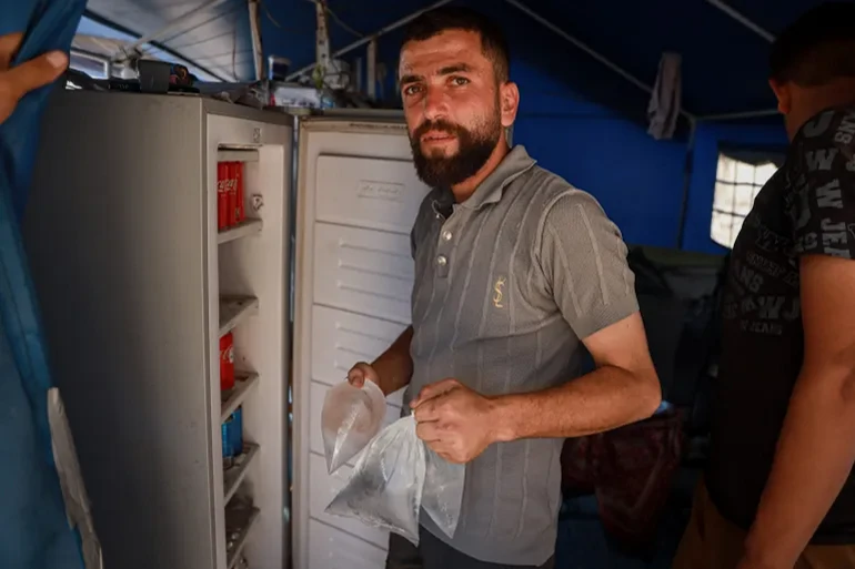 Muhammed el-Zaanin, Gazze şehrinin merkezindeki bir kampta, yerinden edilmiş aileler için ücret karşılığında su torbalarını, içecekleri ve diğer malzemeleri soğutan bir dondurucu hizmeti işletiyor.