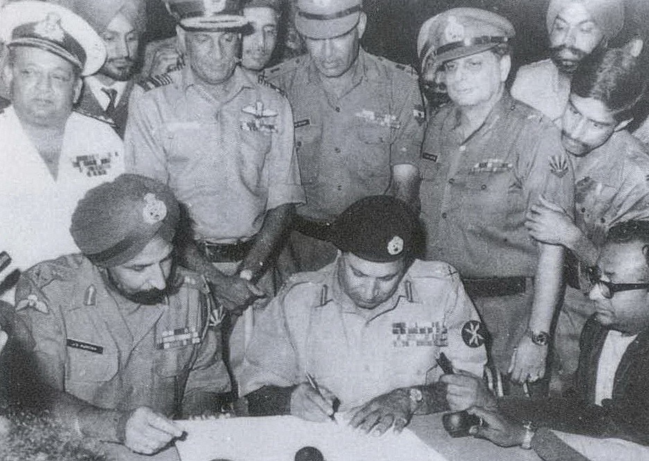 Korgeneral Amir Niazi, Korgeneral Jagjit Singh'in huzurunda Pakistan'ın Hintli ve Bangladeşli güçlere teslim olma belgesini imzalarken, 1971.