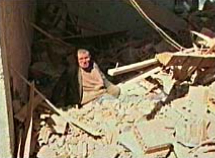 Konvoyların vurulduğu yerin yakınındaki evinin enkazında oturan bir adam.